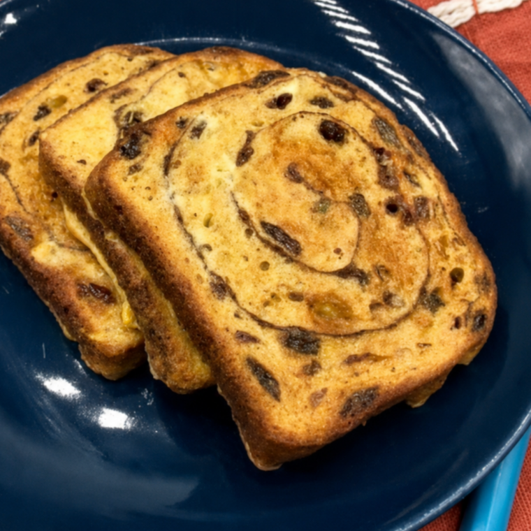 Air fryer cinnamon raisin french toast on a plate with maple syrup, butter, and powdered sugar