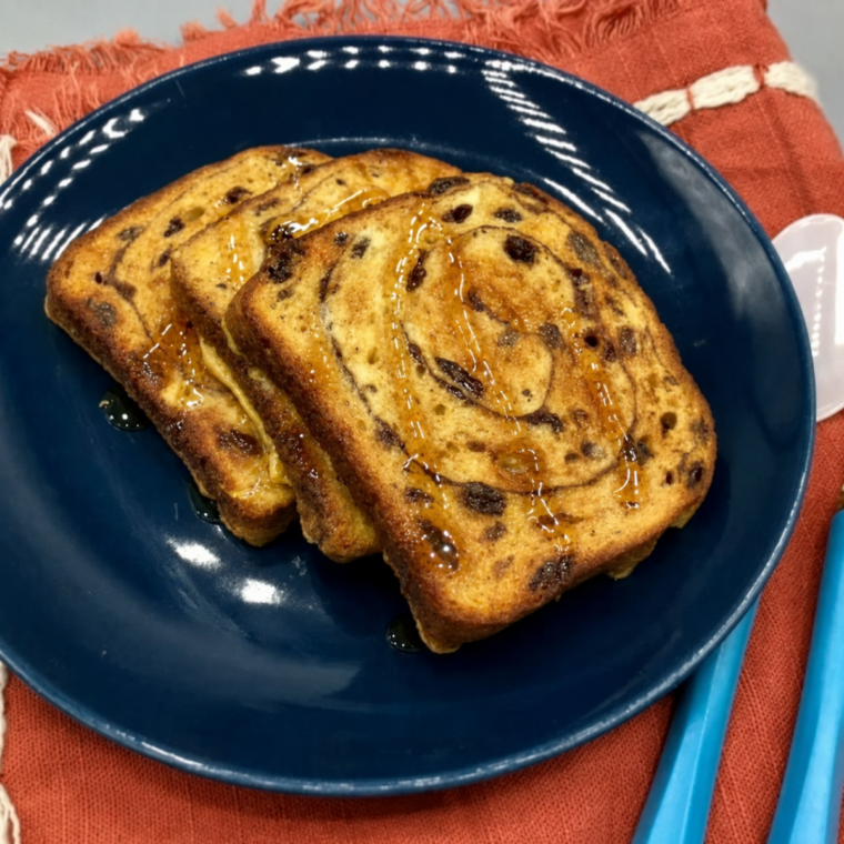 Golden air fryer cinnamon raisin french toast stacked on a white plate with maple syrup and powdered sugar