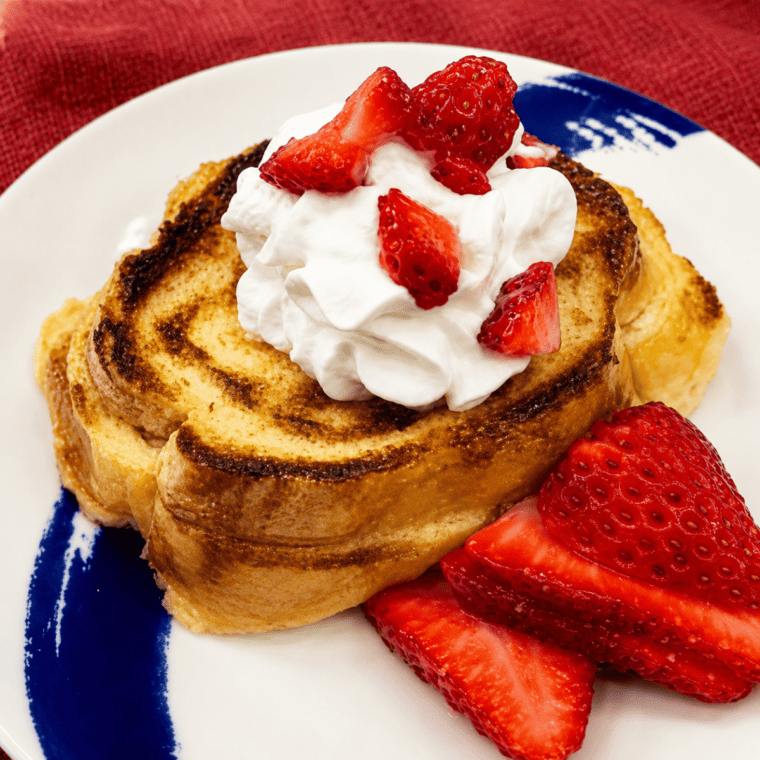 Golden strawberry shortcake French toast served on a white plate with a swirl of whipped cream