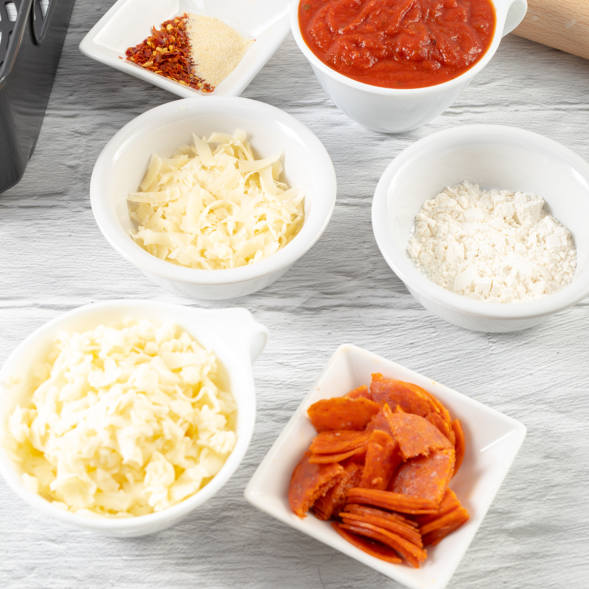 Canned jumbo biscuits, pizza sauce, shredded mozzarella, and pepperoni arranged on a counter