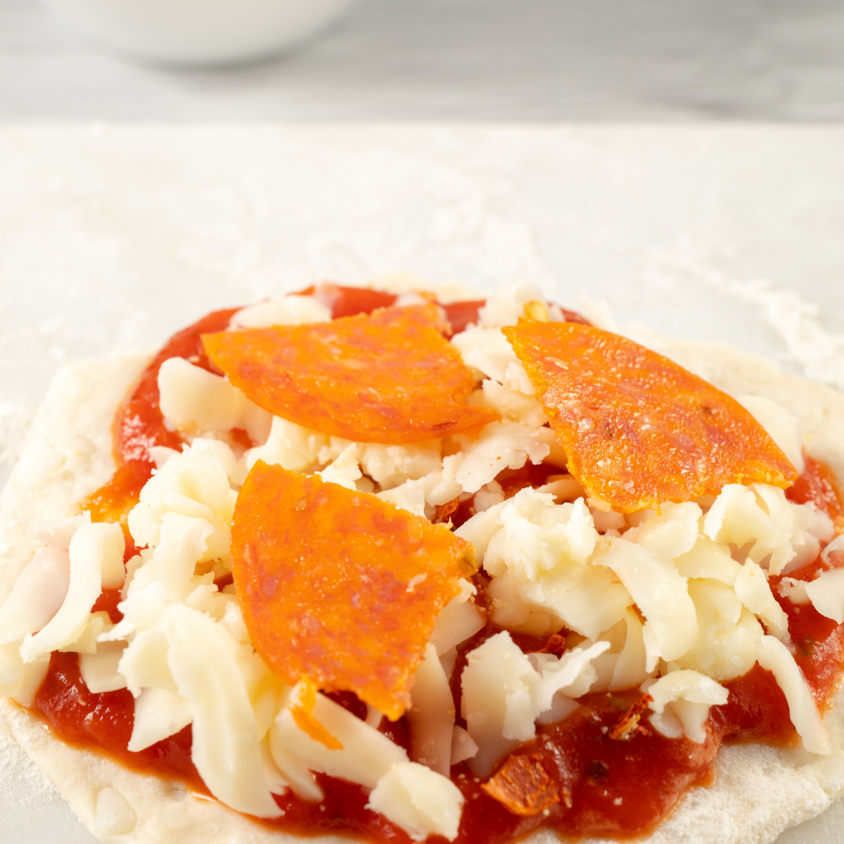 Adding pizza sauce and shredded mozzarella to pre-cooked biscuit pizza crusts