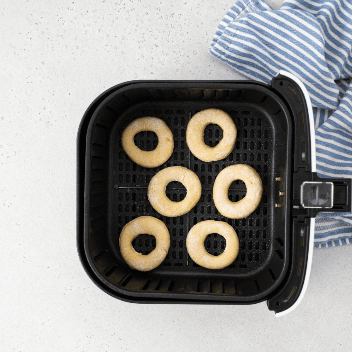Fresh donuts cooking in an air fryer basket until golden.