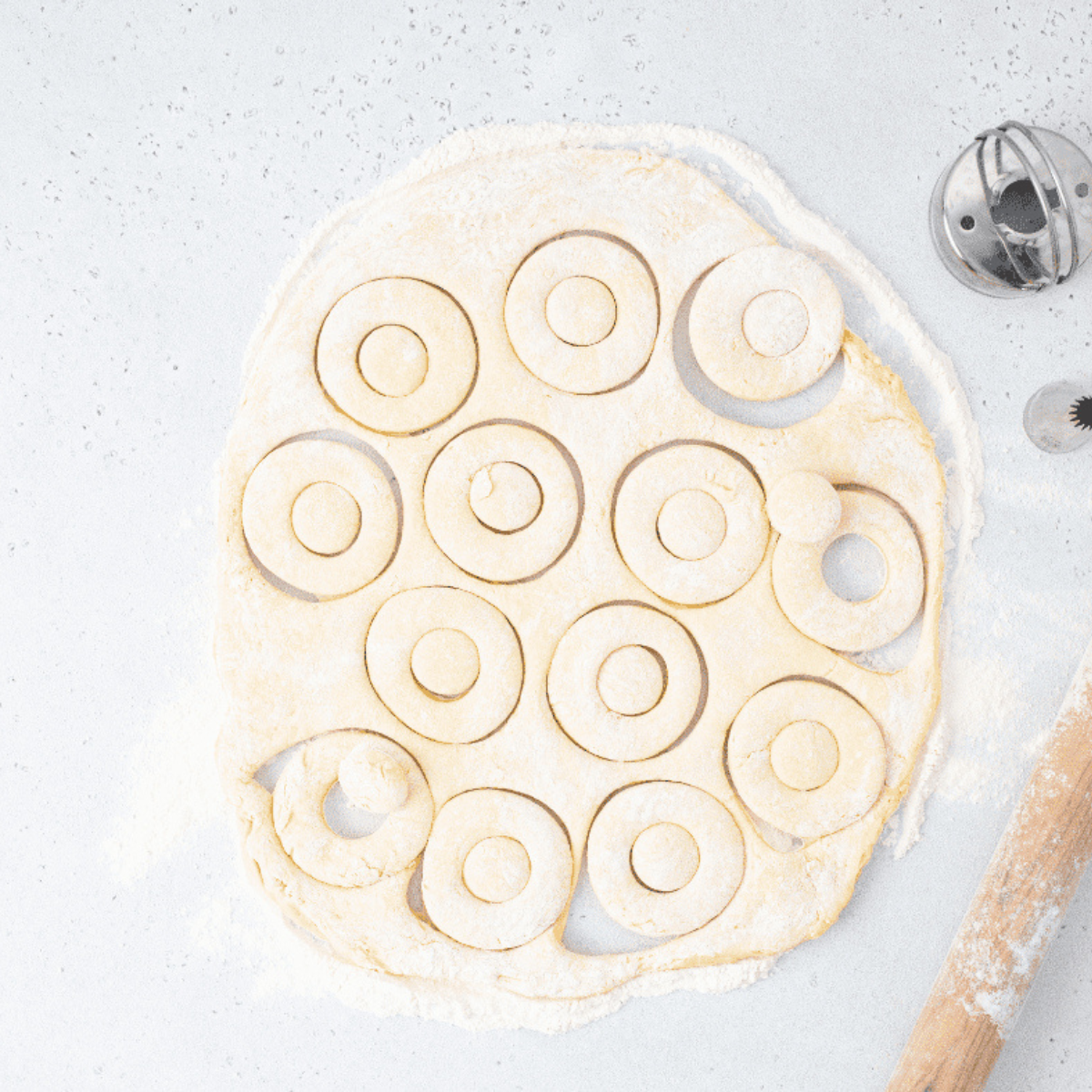 Rolled-out donut dough on floured surface with biscuit cutters.