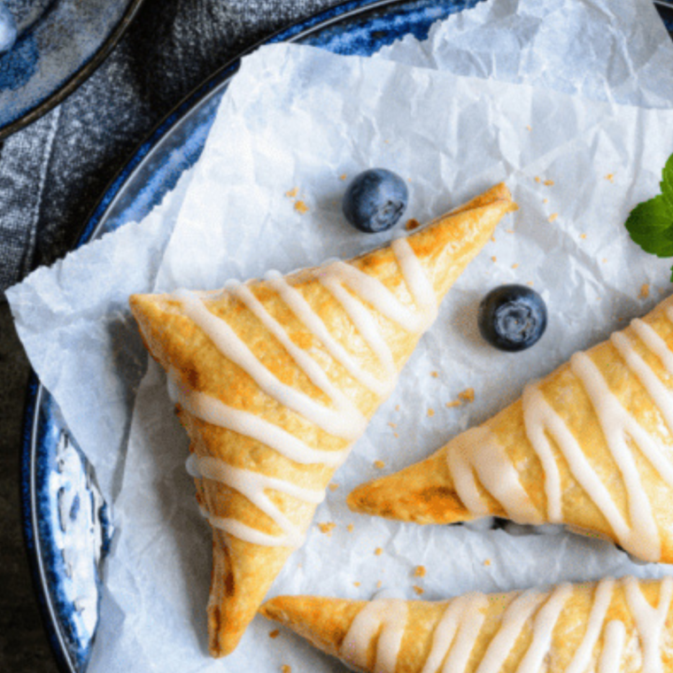 Blueberry puff pastry turnovers arranged in air fryer basket, cooking to golden brown.