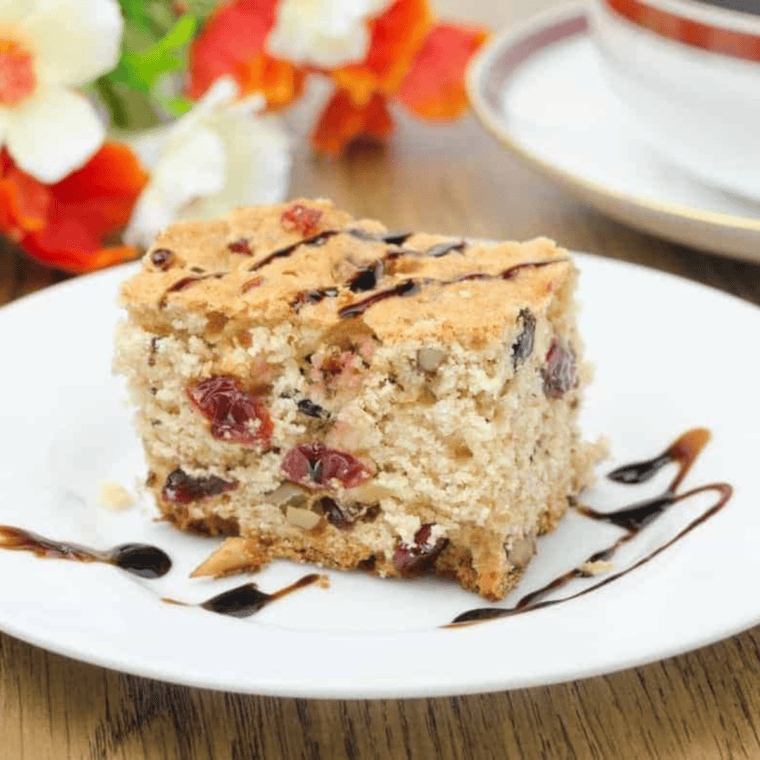 Air Fryer Cranberry and Walnut Bundt Cake, golden brown with cranberries and walnuts on top, served on a white plate.