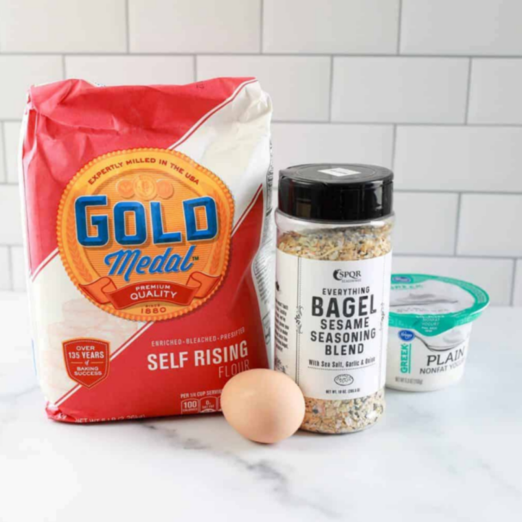 Ingredients for Air Fryer Cheddar Cheese Bagels including Greek yogurt, self-rising flour, shredded sharp cheddar cheese, egg, and salt in prep bowls.