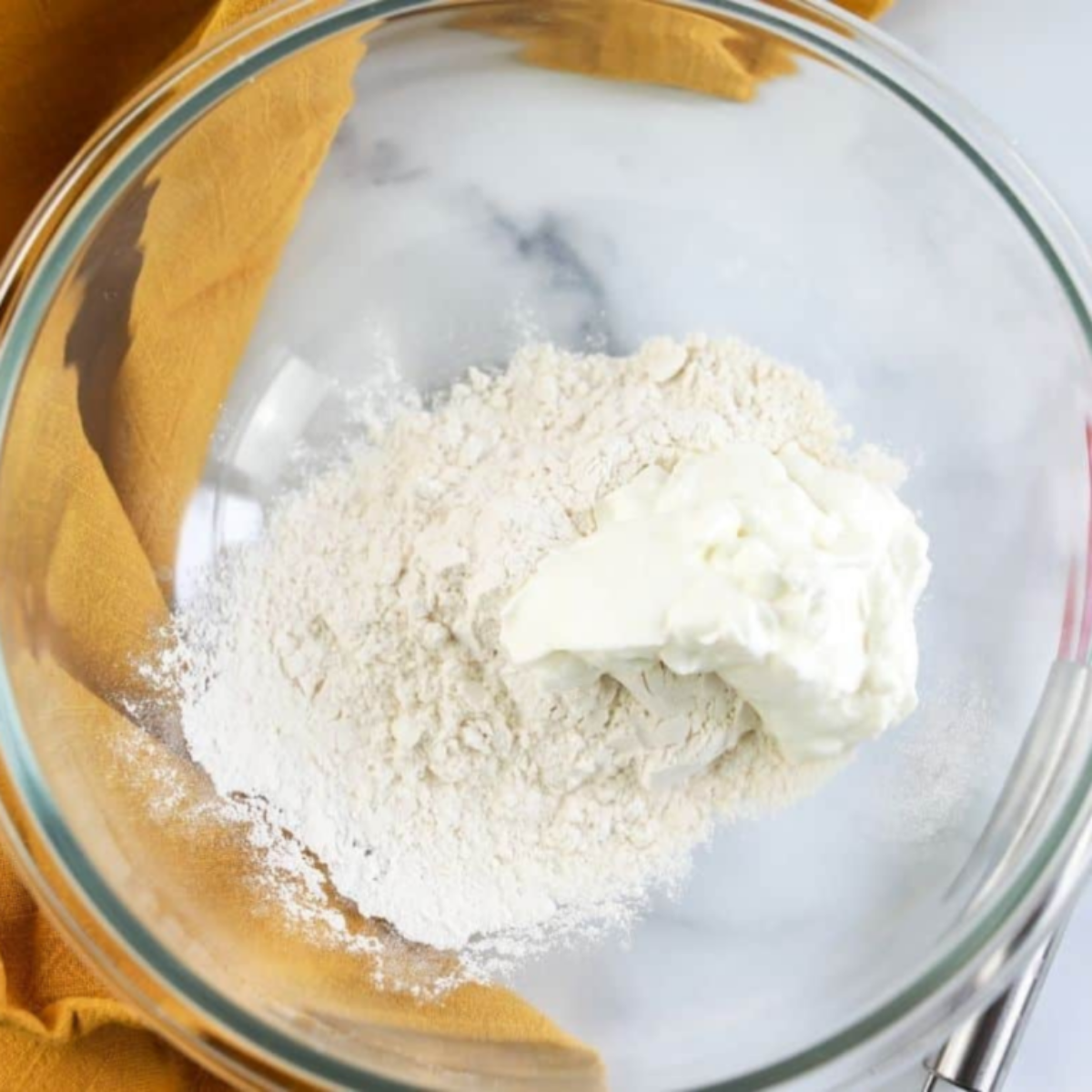 Mixing Greek yogurt and self-rising flour together in a glass bowl to form Air Fryer Cheddar Cheese Bagel dough.