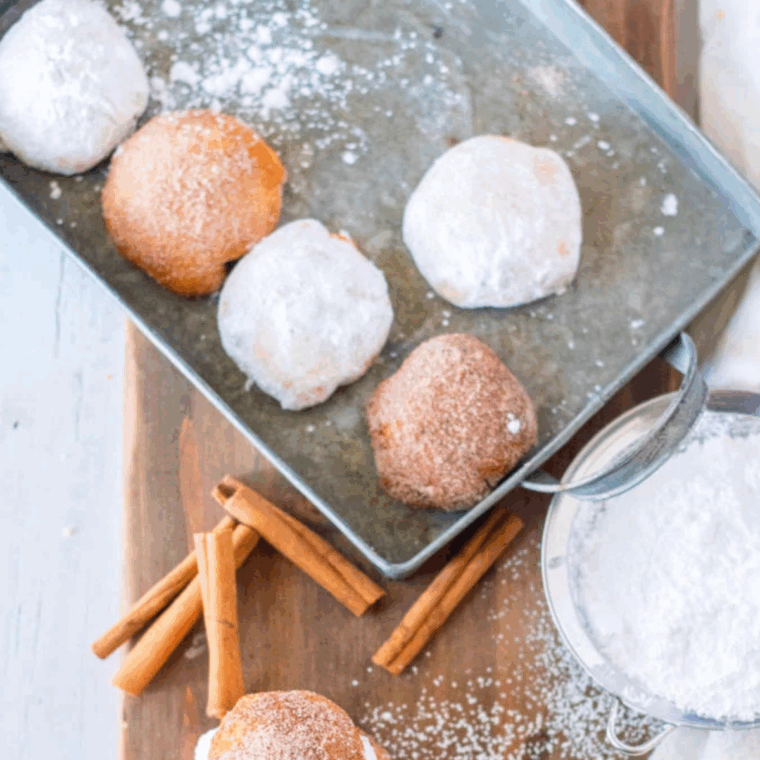 Golden air fryer donut holes coated with powdered sugar, served on a plate.