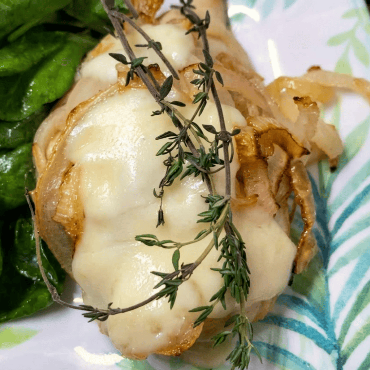 Air fryer French onion chicken breast topped with roasted onions and melted Fontina cheese on a white plate