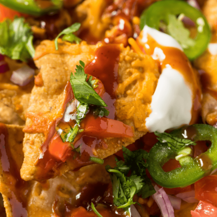 Loaded BBQ pork nachos with melted cheese, smoky pulled pork, BBQ sauce, jalapeños, sour cream, and fresh toppings served over crispy tortilla chips for sharing.