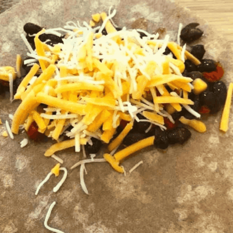 Sprinkling shredded cheese over black bean and corn filling on tortilla