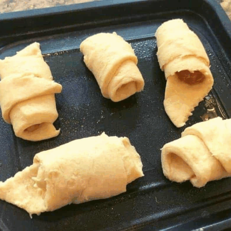 Air fryer basket sprayed with cooking spray, holding unbaked apple pie crescents.