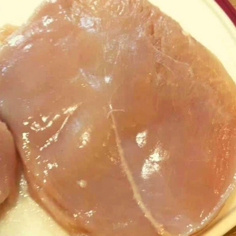 A boneless chicken breast being sliced horizontally into two thin cutlets with a chef's knife