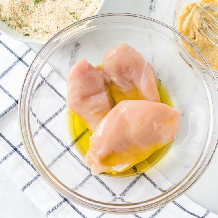 Chicken cutlet under plastic wrap being pounded to an even half-inch thickness with a meat mallet