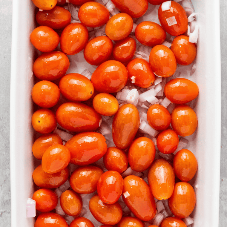 Cherry tomatoes tossed with olive oil and Italian seasoning in a glass mixing bowl