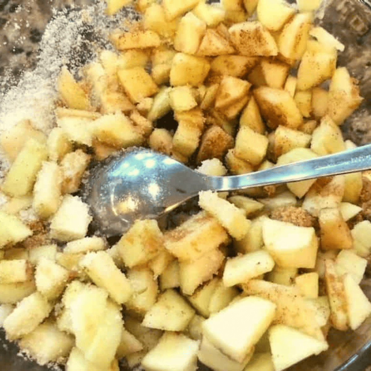 Apple slices mixed with sugar, cinnamon, nutmeg, lemon juice, and cornstarch in a bowl.
