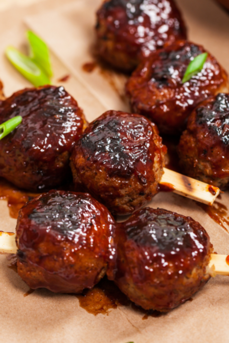 Glazed BBQ meatballs cooking in an air fryer basket, coated in sticky sauce and caramelized on the edges.