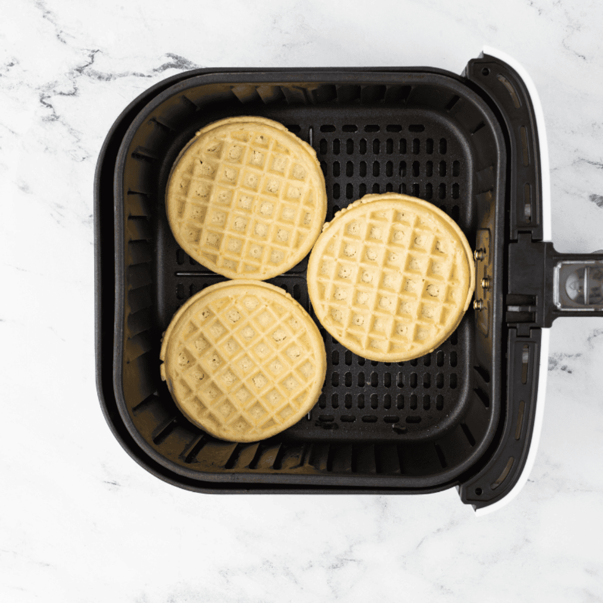 Two frozen waffles placed in a single layer inside a black air fryer basket to ensure proper airflow.