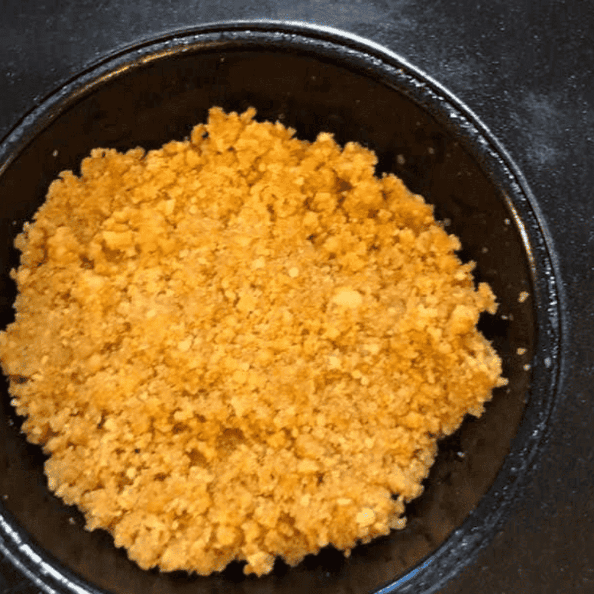 Pressing a graham cracker, sugar, and butter mixture into a greased muffin tin.