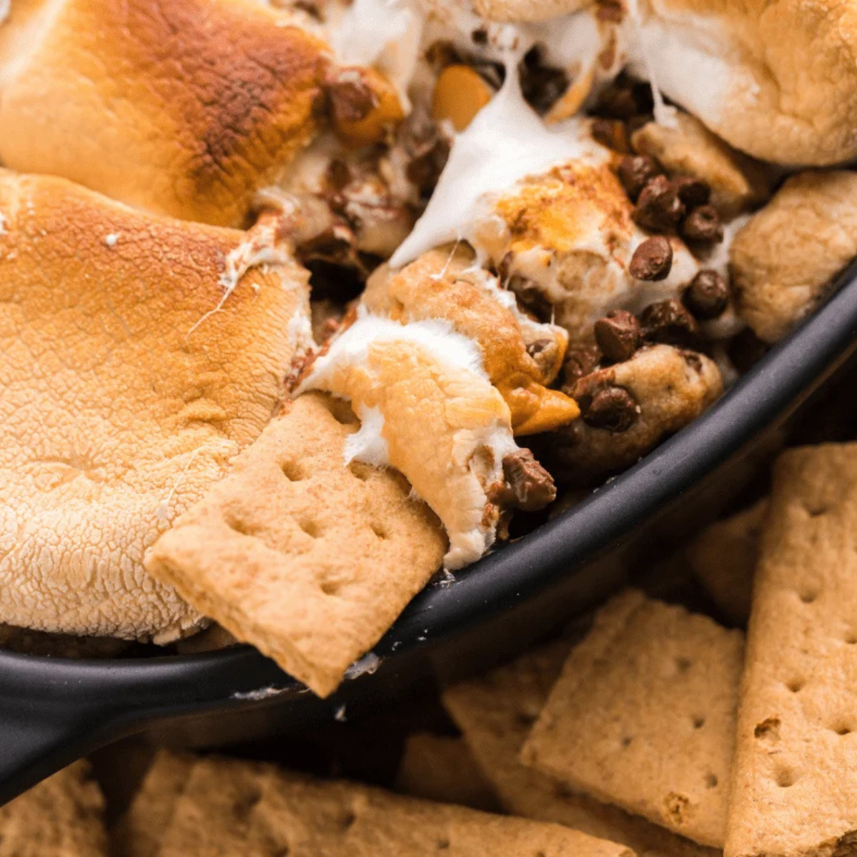 overhead closeup of air fryer s'mores dip with golden toasted marshmallows and graham crackers dipped into the melted chocolate