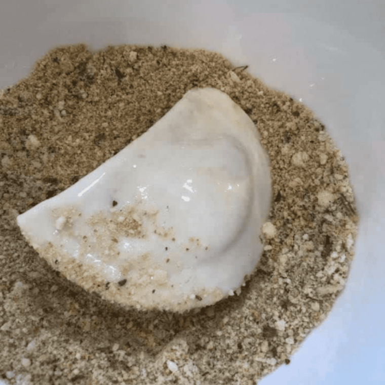 Pierogies being coated with seasoned bread crumbs and grated cheese.