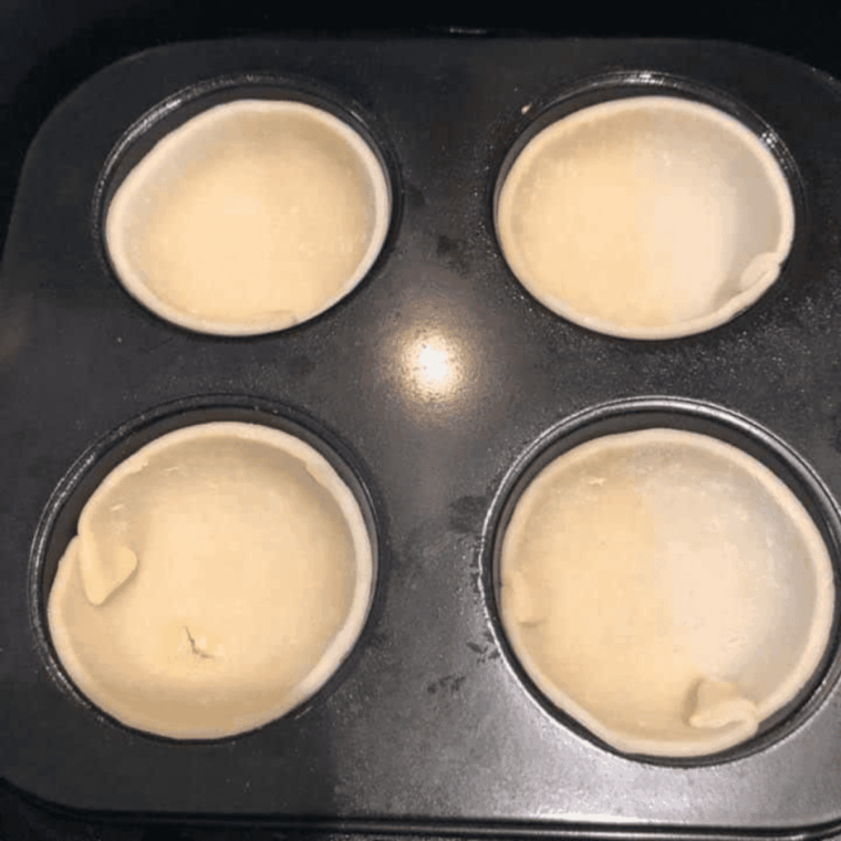 Dough-lined muffin tins placed in the air fryer, cooking until golden brown at 320°F.