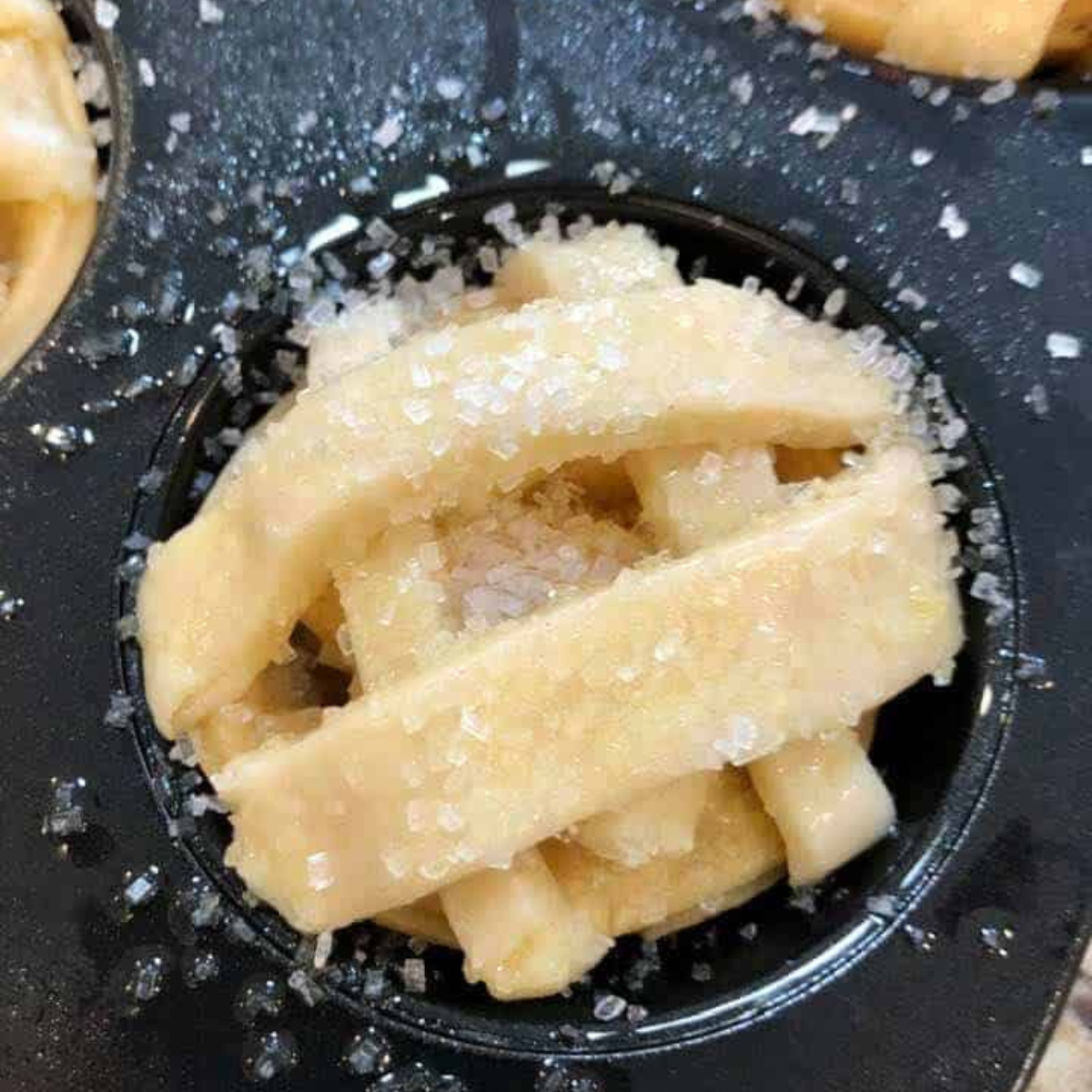 Golden mini apple pies in an air fryer muffin tin with cinnamon apple filling