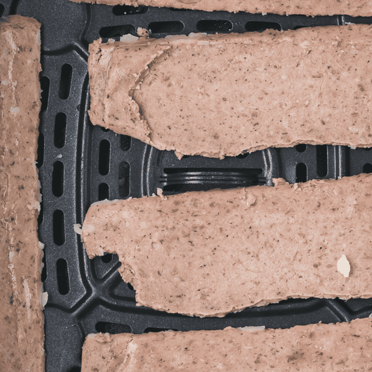 Seasoned beef strips arranged in an air fryer basket before cooking.