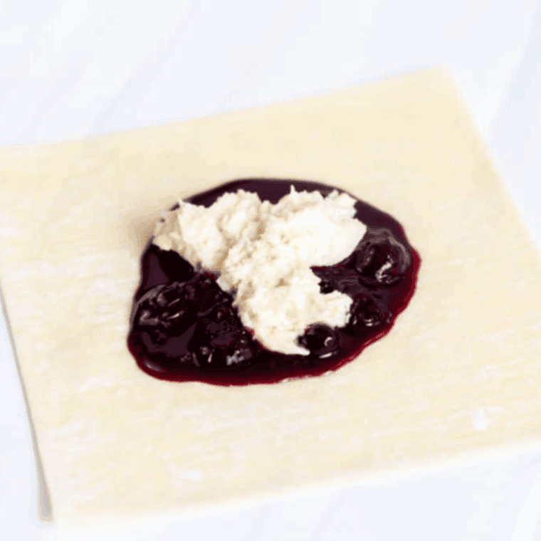 Air fryer basket sprayed with oil, egg roll wrappers filled with blueberry and cheesecake mixture, folded and sealed, ready to cook.