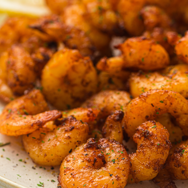 Golden air fryer lemon garlic shrimp garnished with parsley and lemon wedges on a white plate