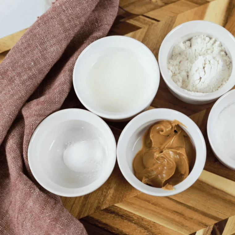 Flour, granulated sugar, baking powder, milk and creamy peanut butter measured into small bowls on a marble surface