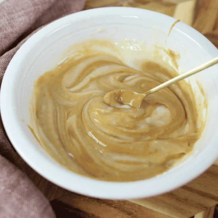 Creamy peanut butter being folded into pale mug cake batter with a silicone spatula