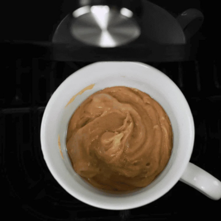 Peanut butter mug cake batter spooned into a greased white ceramic mug before air frying