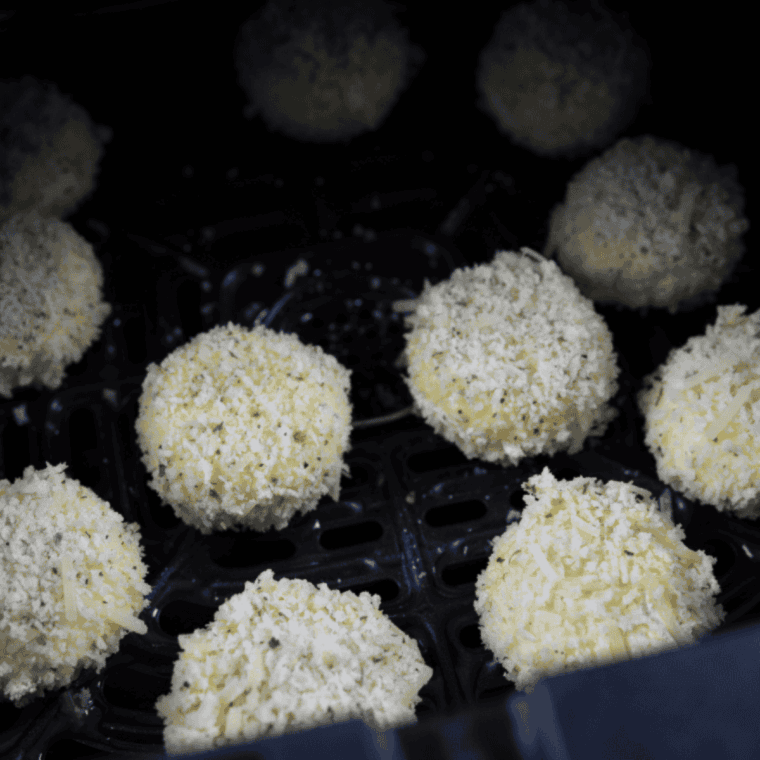 Frozen breaded Babybel cheese rounds placed in a single layer inside the air fryer basket