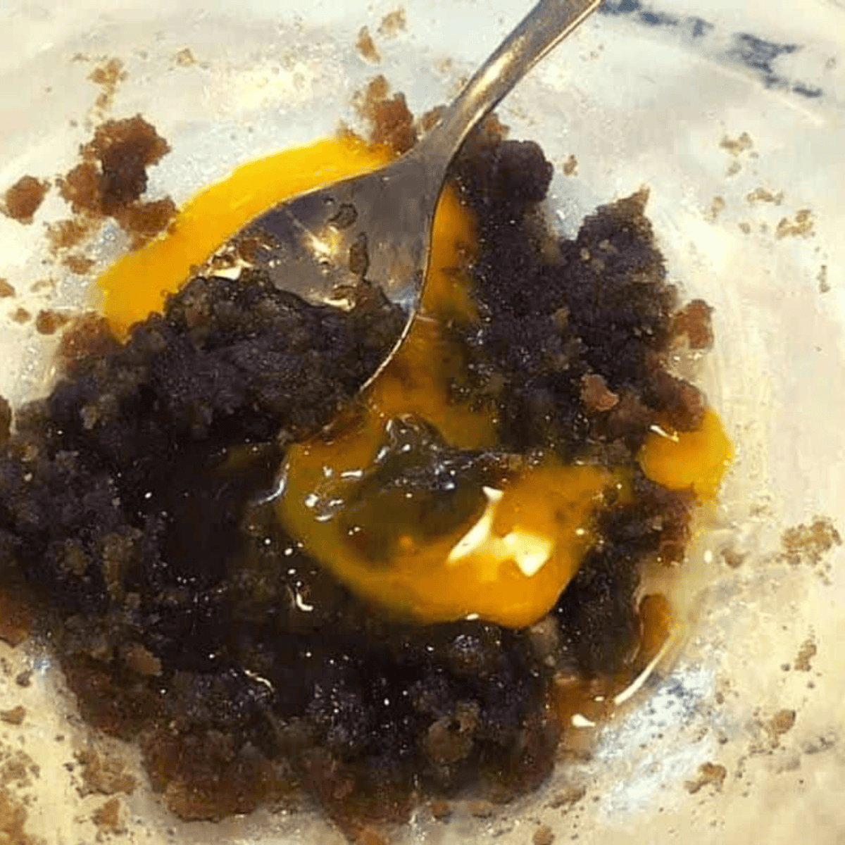 Spraying air fryer pan with olive oil, then mixing melted butter, brown sugar, egg yolks, vanilla, and salt in a bowl until smooth blondie batter forms.