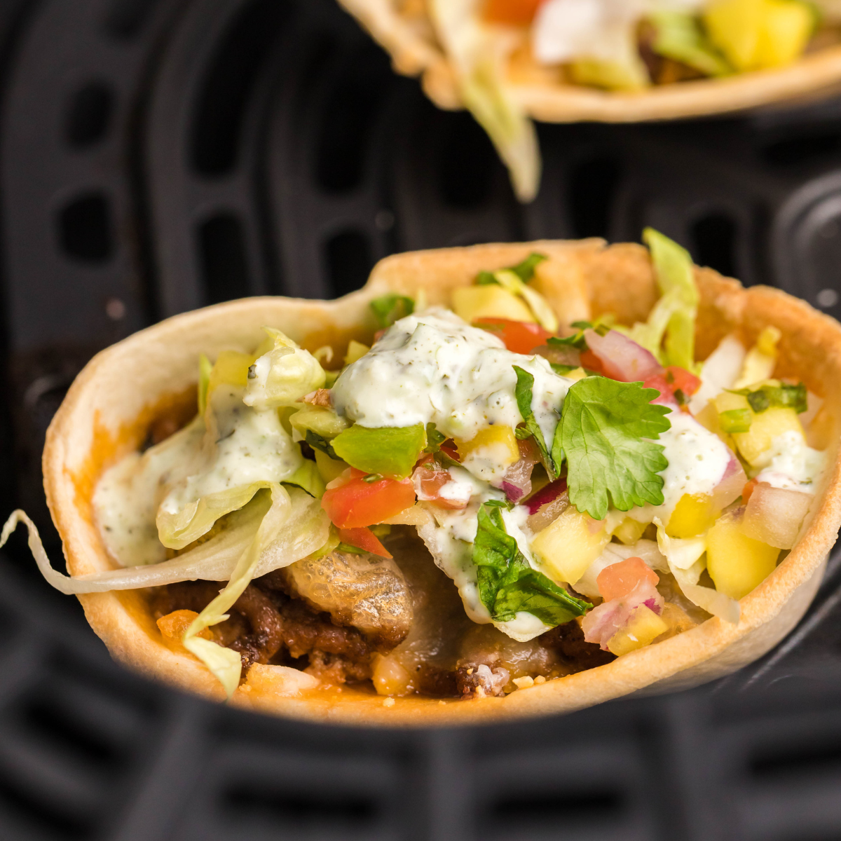 Air Fryer Taco Cups topped with lettuce, pico de gallo, and cilantro lime sour cream.