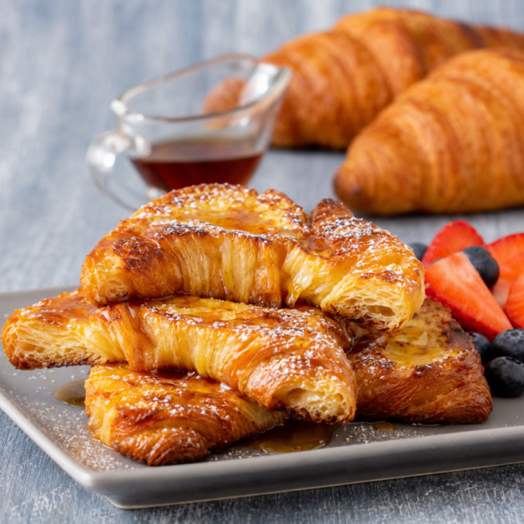 Air fryer croissant french toast topped with roasted strawberries and powdered sugar on a white plate