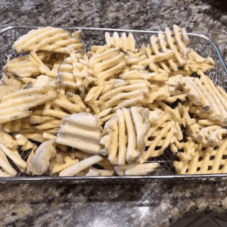 Frozen waffle fries arranged in a single layer in an air fryer basket before cooking