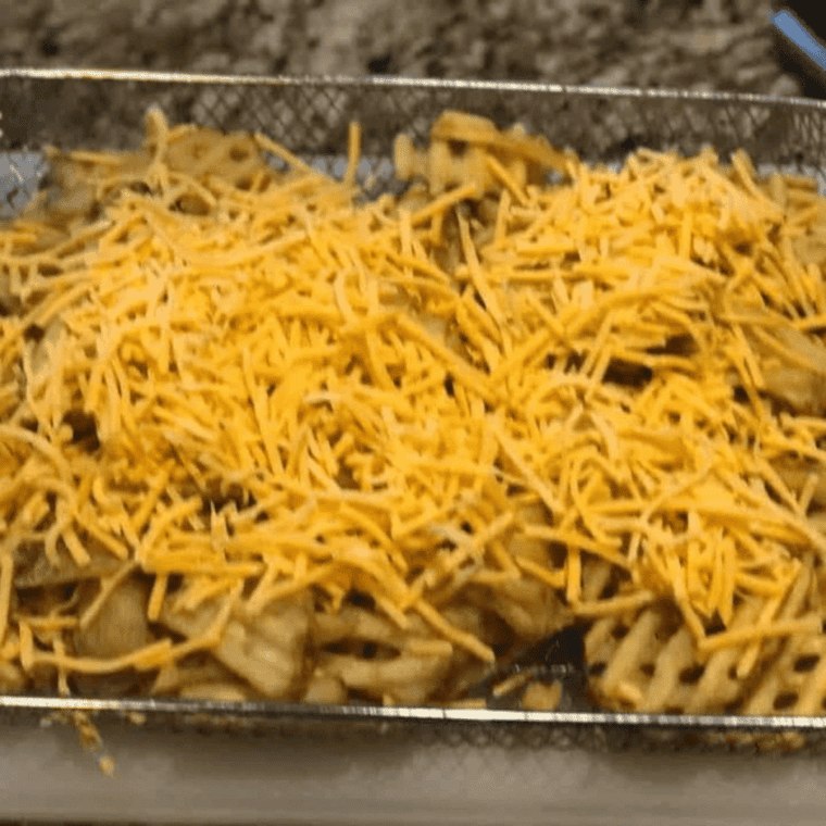 Shredded cheddar cheese melting over crispy waffle fries in an air fryer basket