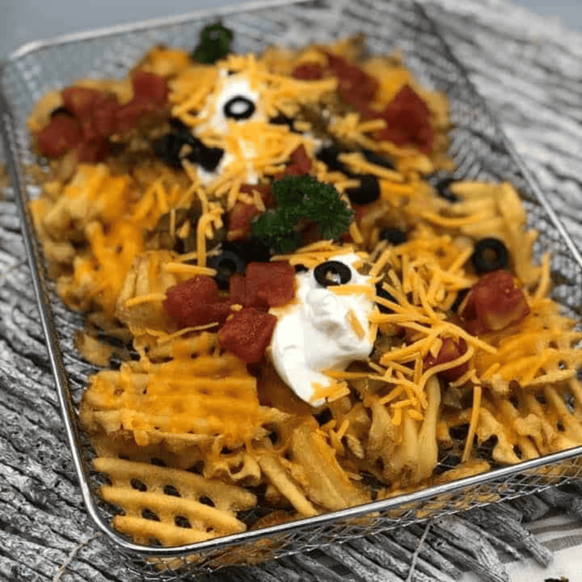 Tray of air fryer loaded waffle fries topped with melted cheddar, crumbled bacon, jalapeños, and green onions