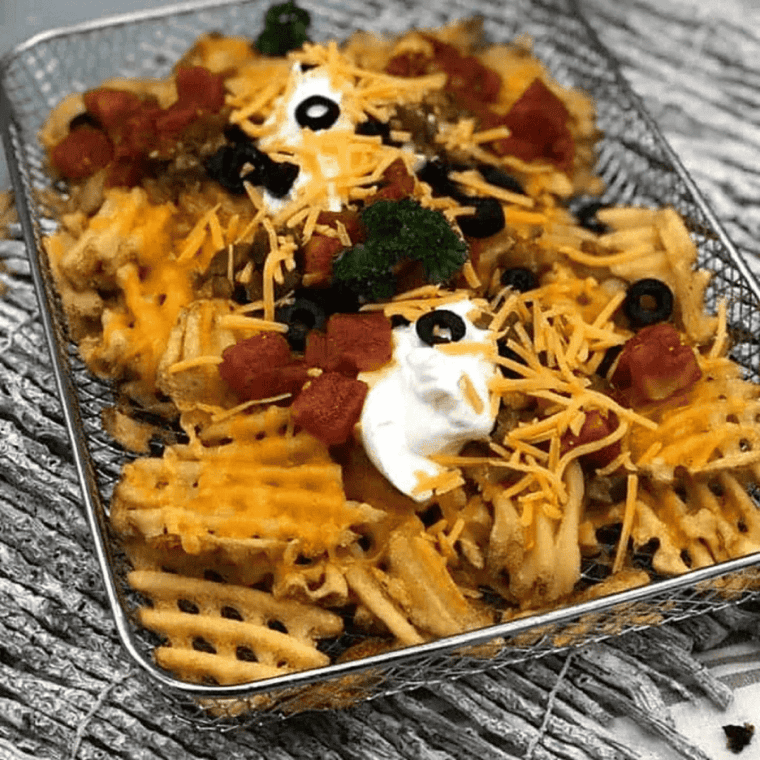 Air fryer loaded waffle fries topped with melted cheddar, bacon, jalapeños, and sour cream on a white platter