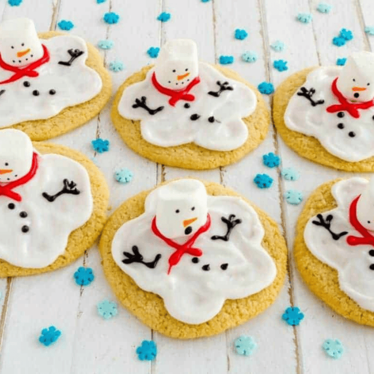 Whimsical melting snowman cookies with a soft white icing "puddle," a puffy marshmallow head, and a tiny orange icing carrot nose on an air-fried sugar cookie.