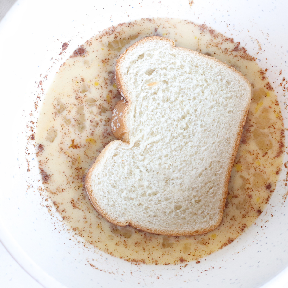 Thick brioche slice soaking in orange pumpkin custard