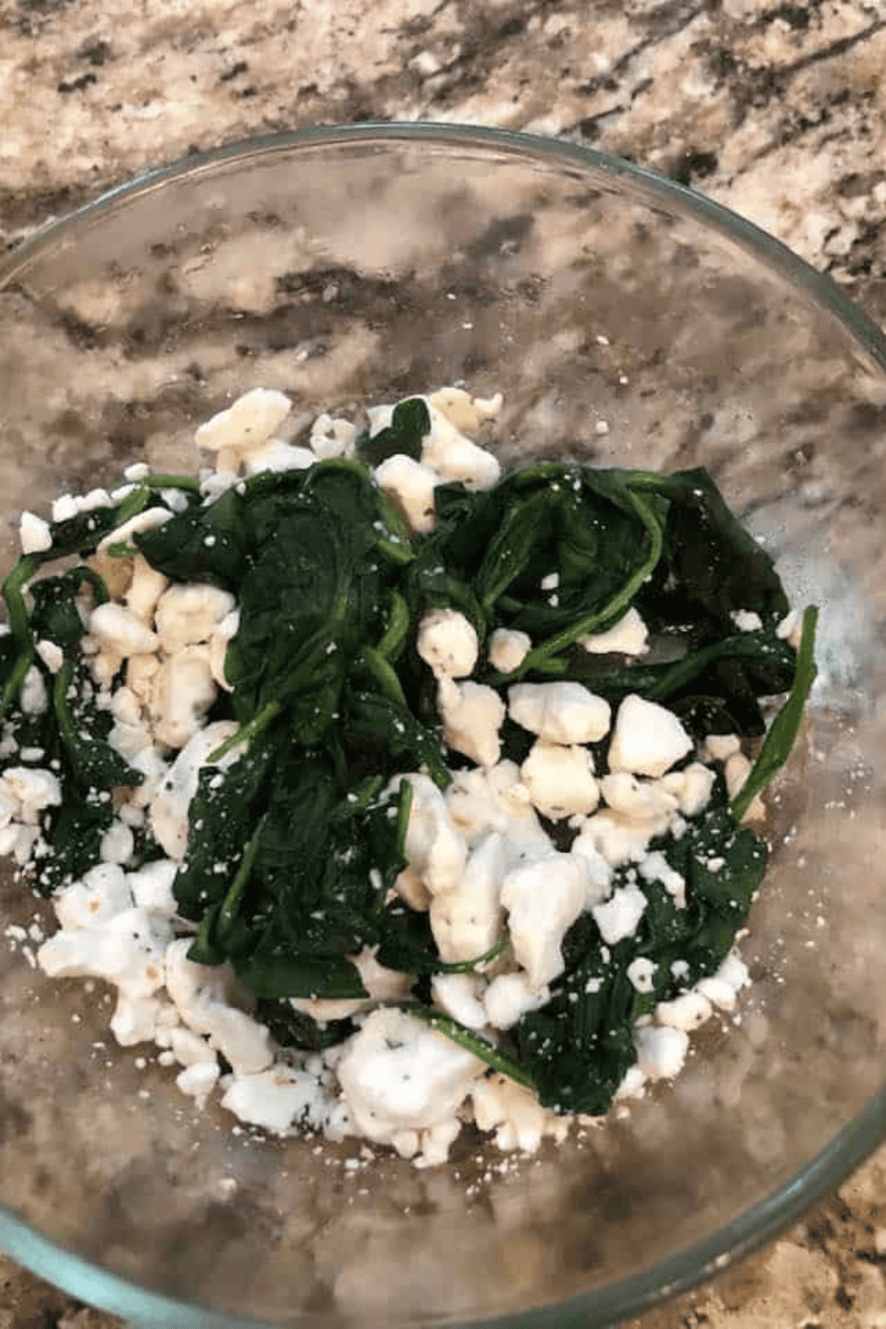 Small mixing bowl with crumbled feta, wilted spinach, salt, and black pepper being combined.