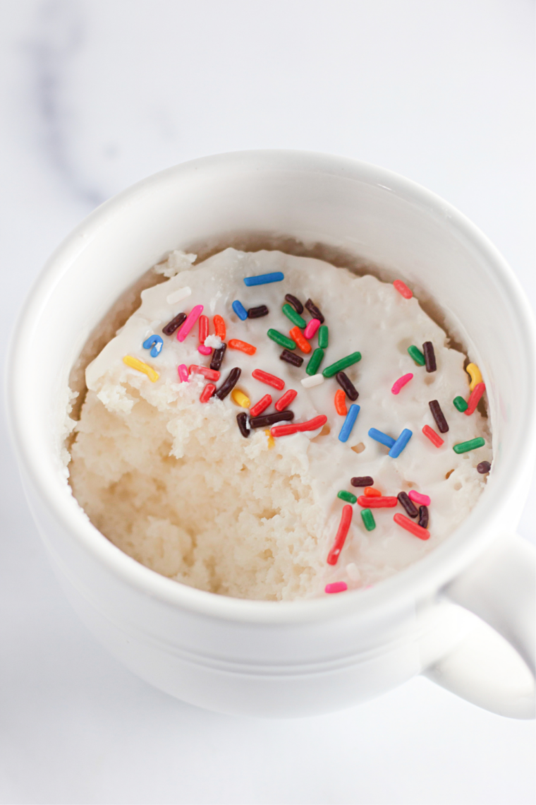 Air fryer vanilla mug cake with icing drizzled over the top and rainbow sprinkles in a white mug