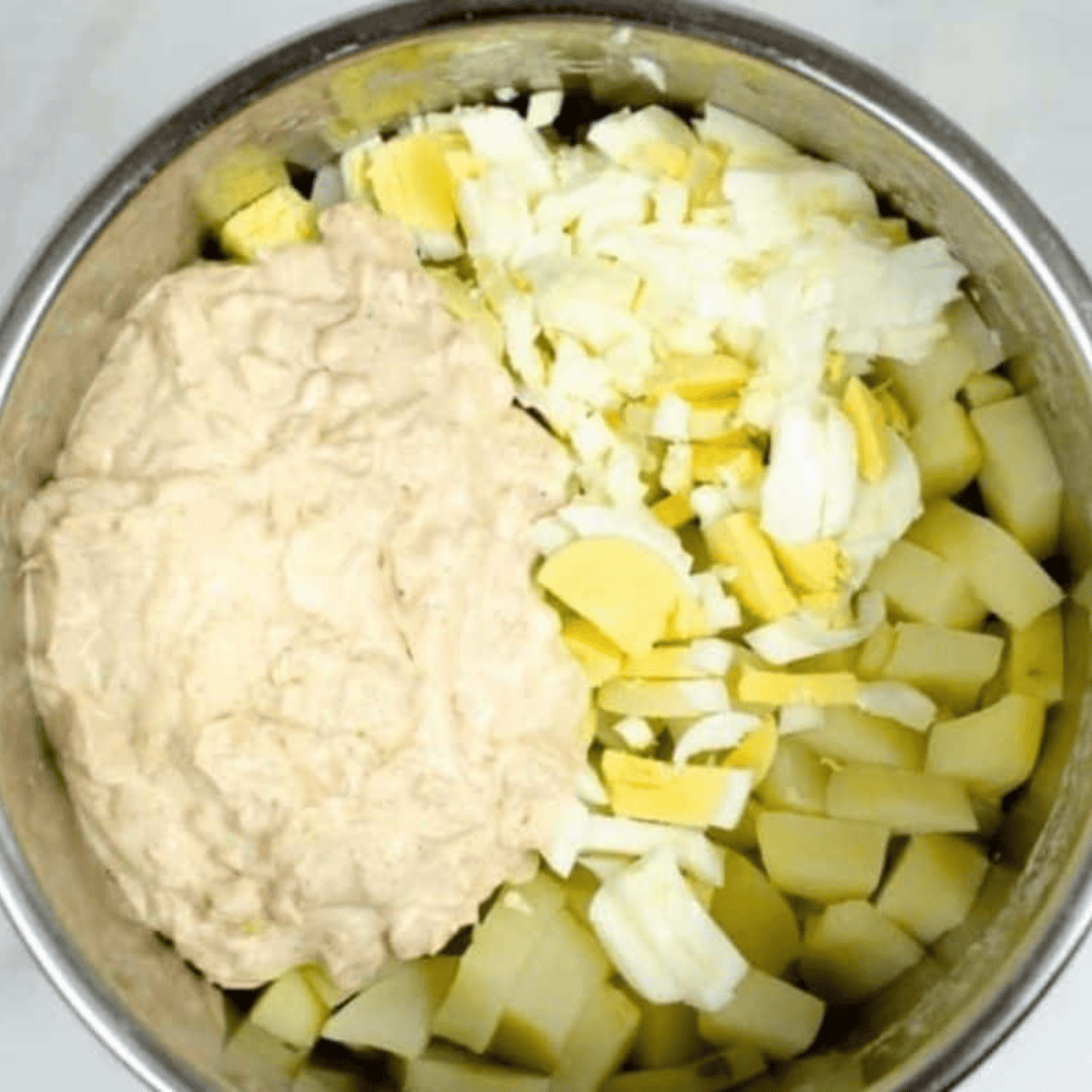 Peeled and chopped eggs, drained potatoes, and chopped onions mixed with mayonnaise and seasonings in the Instant Pot, ready to combine.