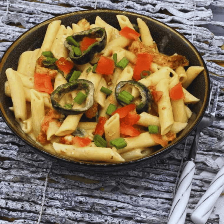 Creamy Instant Pot Cajun Chicken Alfredo served with penne pasta, sliced chicken, parmesan cheese, and Cajun seasoning in a white bowl.