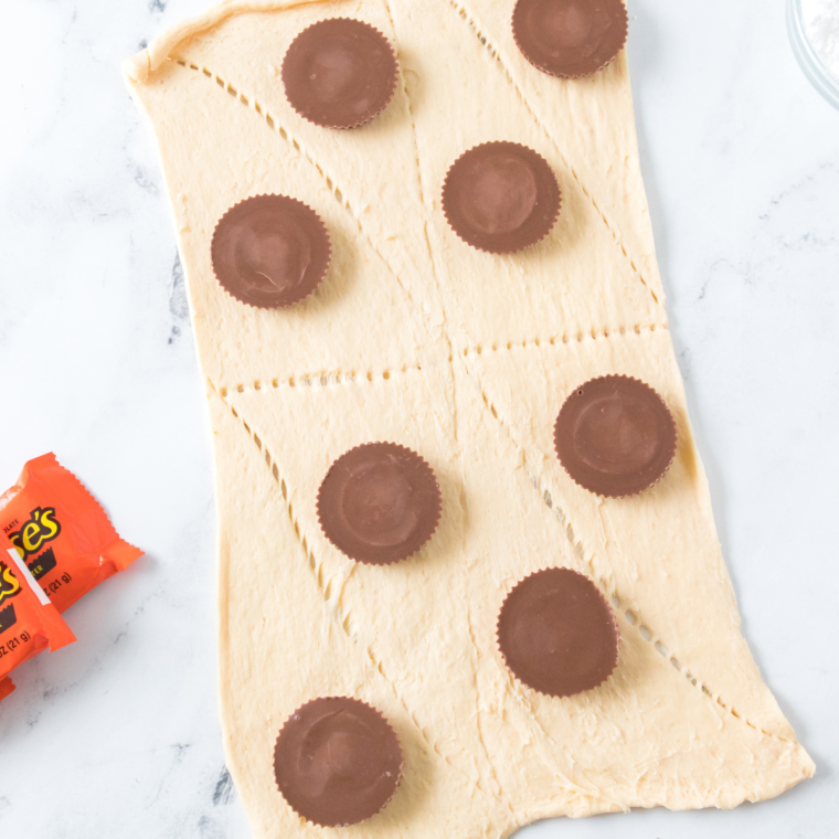A frozen Reese’s cup is placed on the dough and fully wrapped, then seams are tightly pinched shut to seal in the filling. The dough is shaped into a smooth ball to prevent any gaps where chocolate could escape.