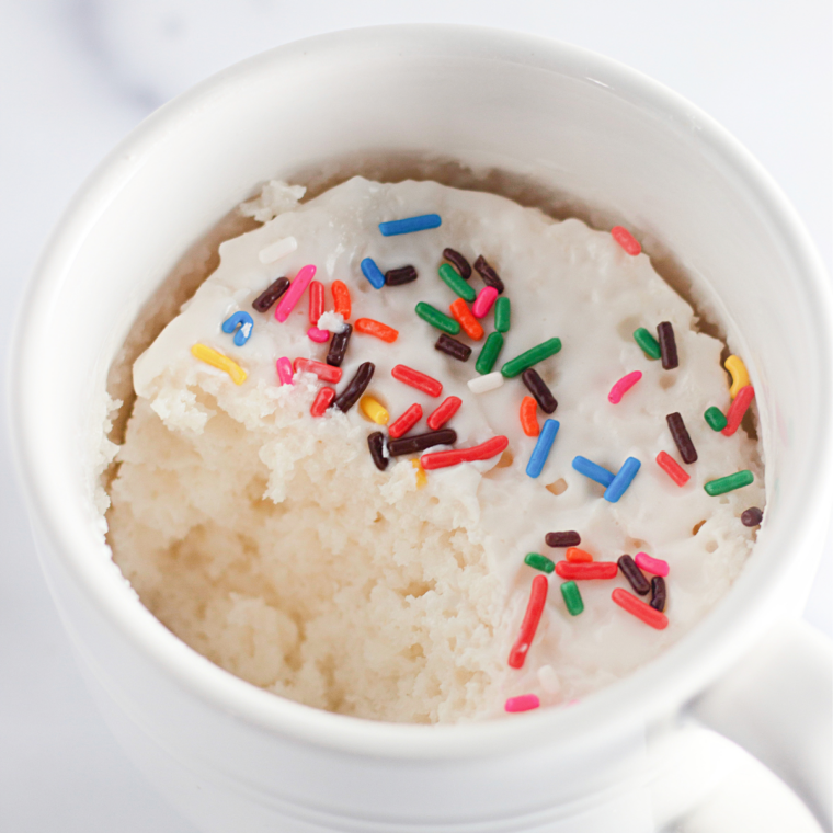 Vanilla icing being drizzled from a spoon over a cooled air fryer mug cake