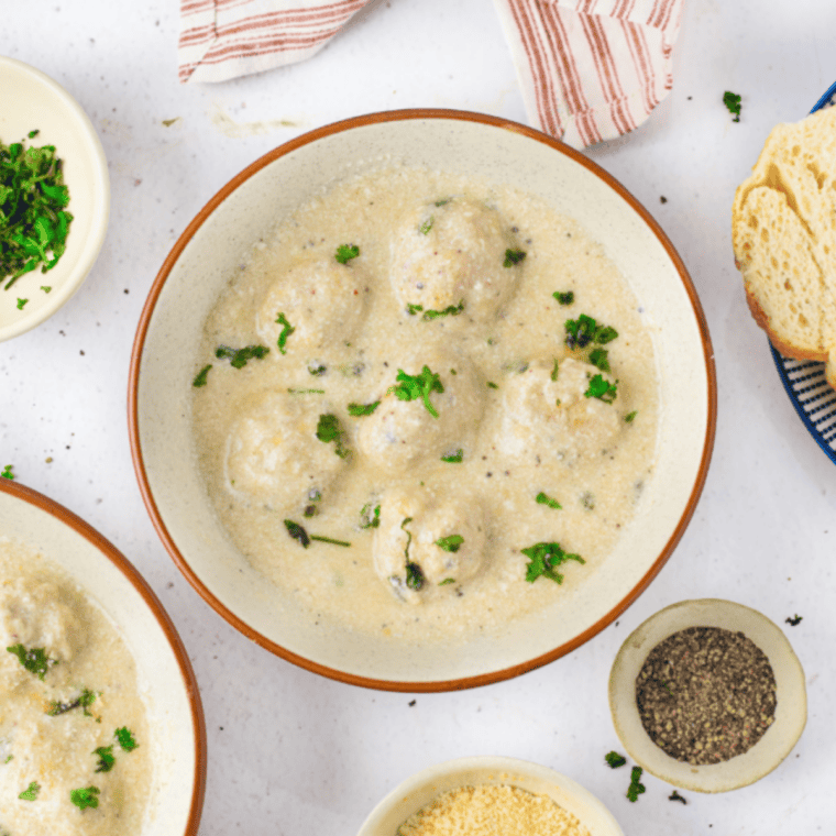 Creamy Alfredo meatballs over fettuccine in a white bowl, garnished with parsley and Parmesan